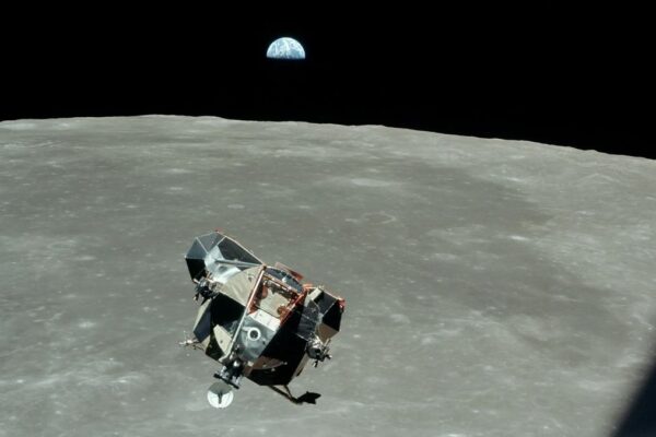 A photo of a moon lander flying over the moon, with Earth far in the background