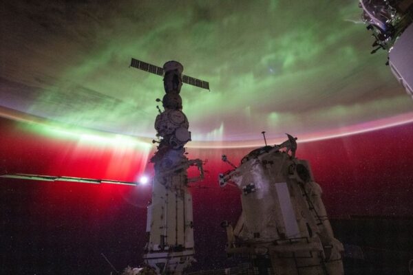 the earth with a large aurora shining on it. in front is the international space station in shadow