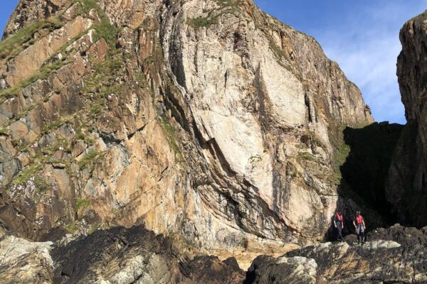 A large rock outcropping with two people walking along the bottom