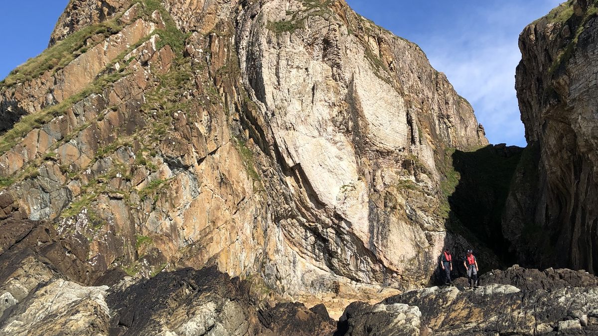 A large rock outcropping with two people walking along the bottom