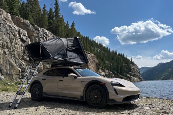 an SUV with a pop tent on top and a ladder in front of a mountain lake