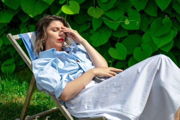 A woman sits on a lounger on a sunny day and holds her head in pain