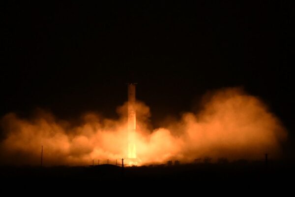 A rocket launches in the dark with an orange glowing cloud beneath it