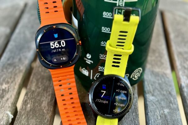 The Garmin Forerunner 965 and Samsung Galaxy Watch Ultra sitting in front of a bottle of water, both showing their respective hydration apps.