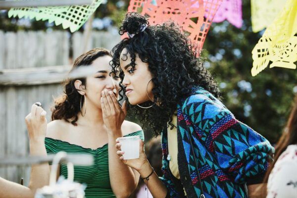 At an outdoor party, a woman whispers in the ear of her friend