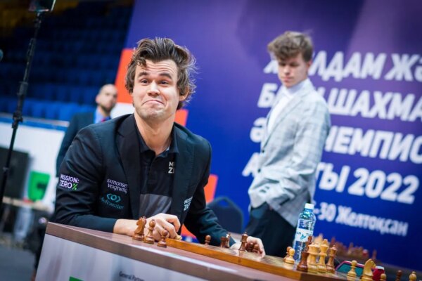 Magnus Carlsen grins while sitting at a table playing chess at the 2022 World Chess Rapid & Blitz Tournament.