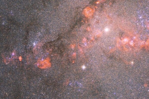 hubble telescope photo of a star-packed galaxy filled with orange-red clouds of gas