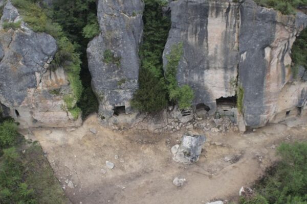 An aerial photo of a tall cliff wall with cave openings on the bottom