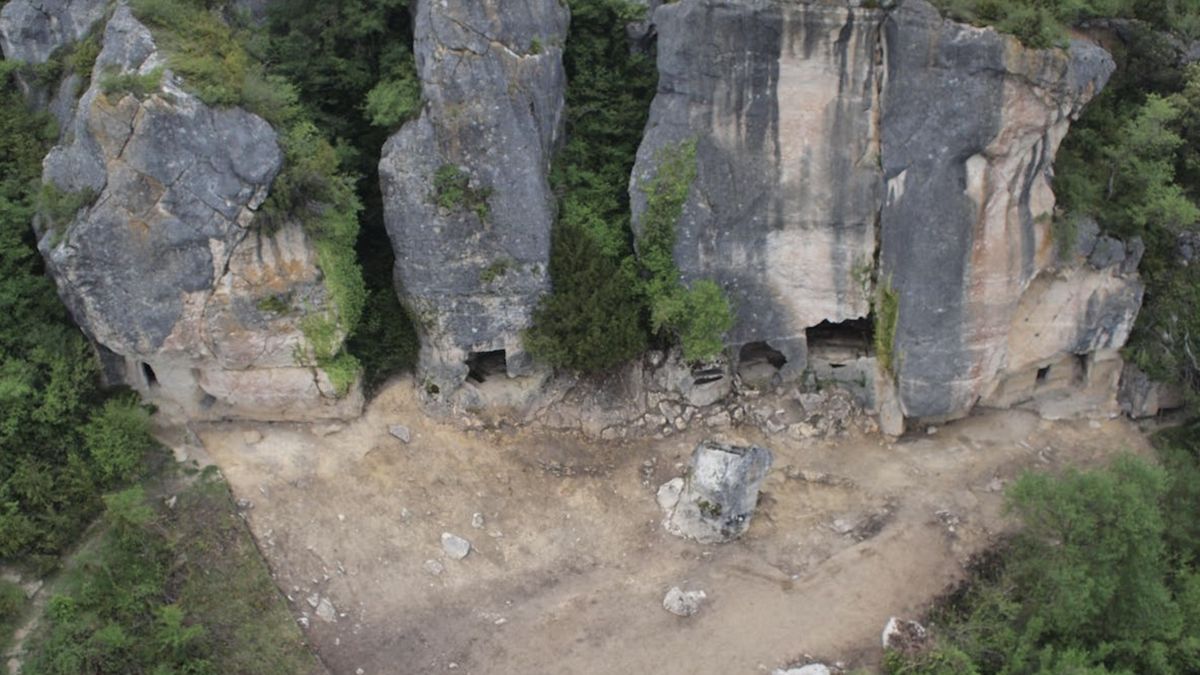 An aerial photo of a tall cliff wall with cave openings on the bottom