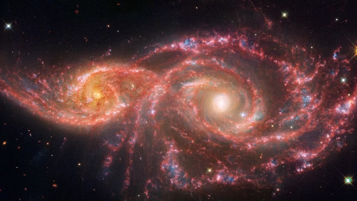 Two intertwined spiral galaxies with a red hue and eye-like shape