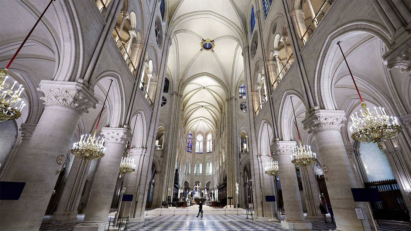 An image inside the Notre Dame cathedral shows a high vaulted ceiling and arches.