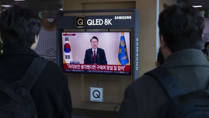 Commuters watch a live broadcast of Yoon Suk Yeol addressing the nation in front of a television at Seoul Station on Thursday